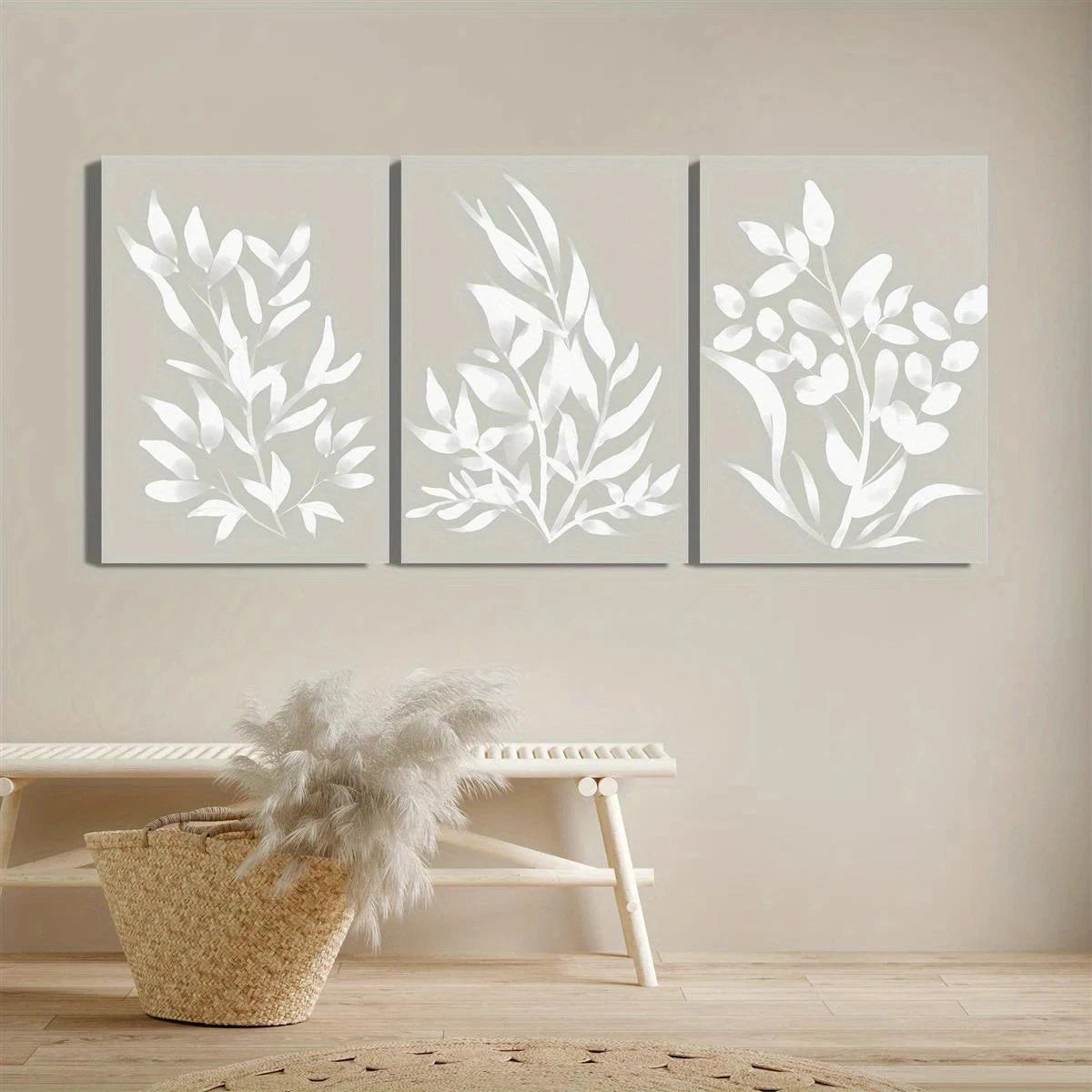 Three framed leaf-patterned wall art pieces on a neutral wall with a woven basket and wooden stool below.