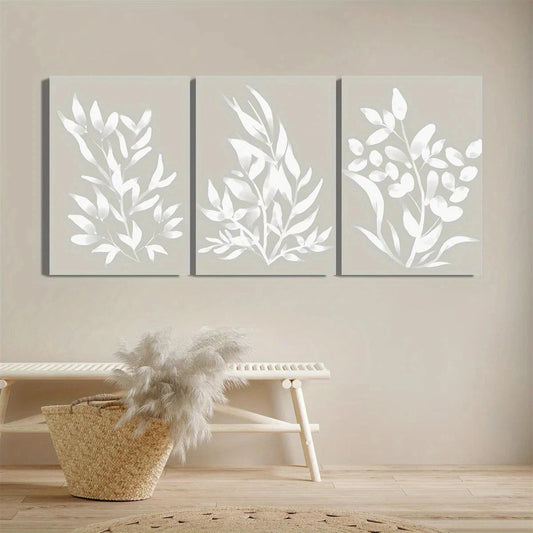 Three framed leaf-patterned wall art pieces on a neutral wall with a woven basket and wooden stool below.