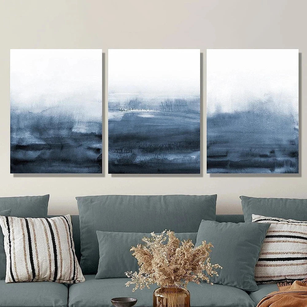 Three abstract wall art pieces above a sofa with decorative pillows and a vase.