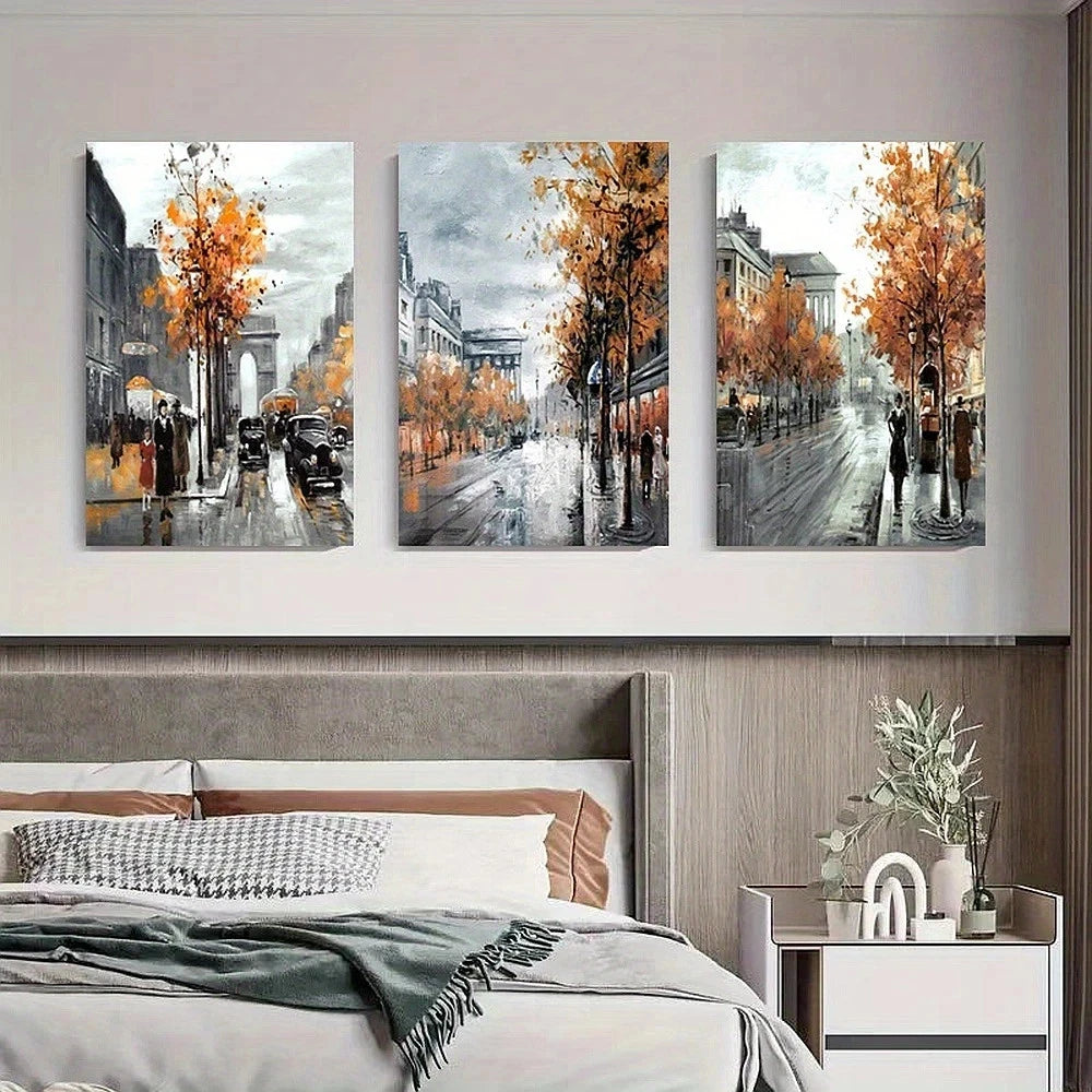 Three framed artworks depicting a city street scene with autumn trees above a bed.