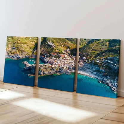 Triptych canvas print of a coastal town with blue water and green hills.