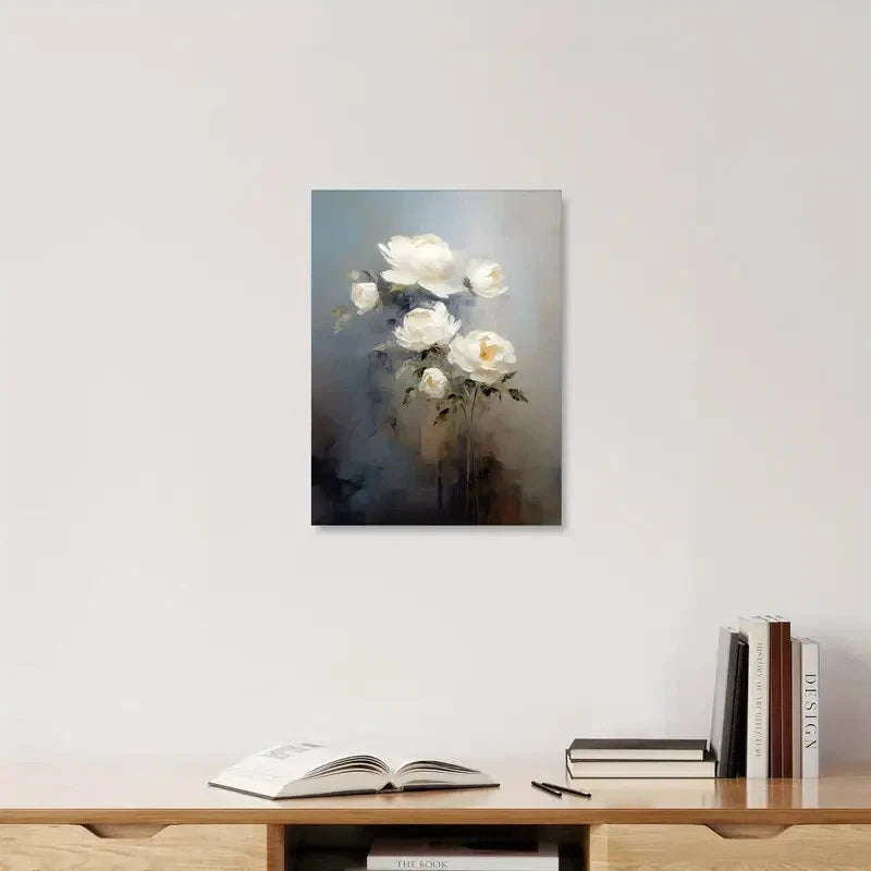 Framed artwork of white flowers on a wall above a shelf with books and an open book.
