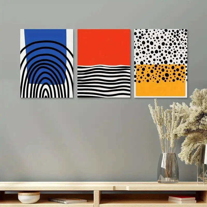 Three abstract art prints on a gray wall above a wooden shelf with decorative items.