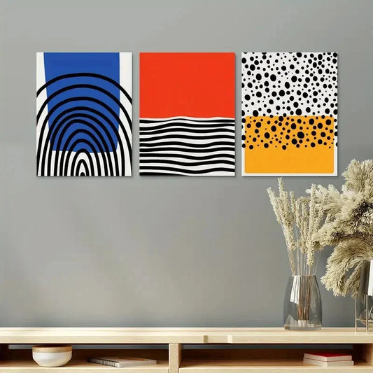 Three abstract art prints on a gray wall above a wooden shelf with decorative items.