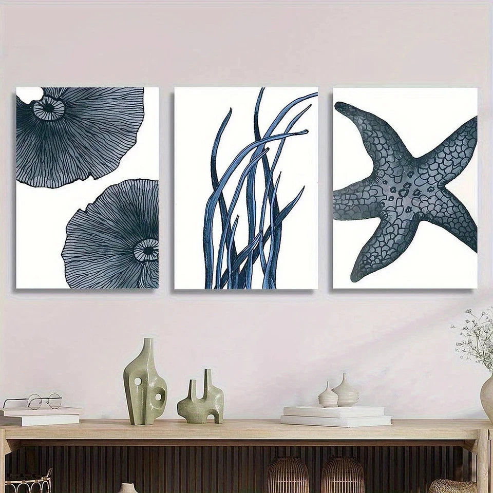 Three coastal-themed wall art pieces on a light pink wall above a wooden shelf.